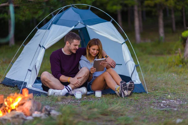 若いカップル コーヒーを飲みながら 山の景色を楽しんで 日没のたき火でタブレットをチェック — ストック写真