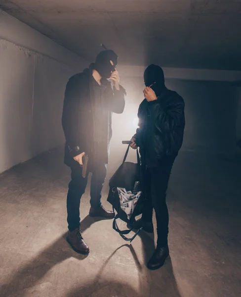 Men with mask standing in dark garage and holding guns and a bag full of money