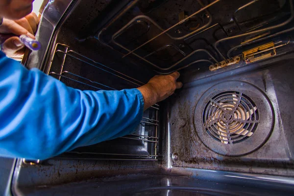 Profesional handyman fixing the motor fan in the oven