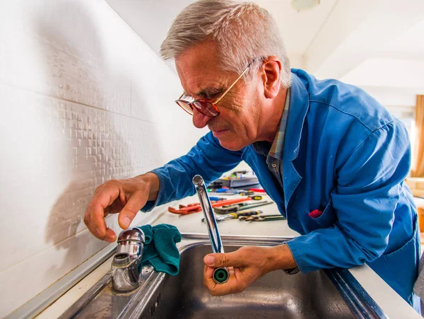 Old age handyman is working in the kitchen, fixing the kitchen tap with his tools