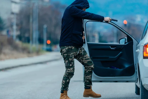 The car thief is pulling the car owner out of his car and trying to get the car while pointing a loaded gun at the drivers head.