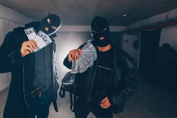 Criminals with masks on their face are holding money in hands and a bag full of money