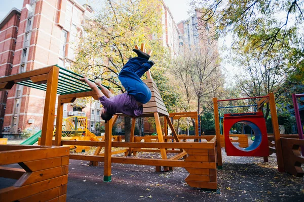 年轻的Parkour小伙子在操场上做手脚 翻筋斗和锻炼 同时从一个秋千跳到另一个秋千 — 图库照片