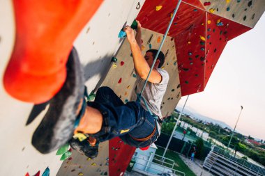 Man climber on artificial climbing wall in bouldering gym clipart