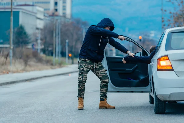 車泥棒は彼の車から車の所有者を引っ張るとロードされた銃のドライバーの頭を指差しながら車を取得しよう — ストック写真