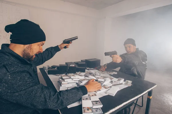 Young criminals are fighting in a room with a pointed gun and money at the table