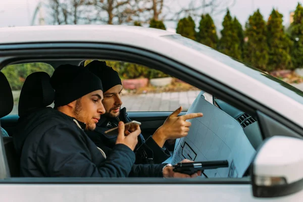 Zwei Diebe parkten in einem wartenden Verbündeten, während sie telefonierten, beobachteten ihr Ziel und luden ihre Waffen. — Stockbild Zwei Diebe Parkten Einem Wartenden Verbündeten Während Sie Telefonierten Beobachteten — Stockfoto