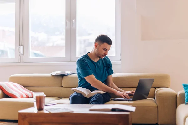 Schöner Student, der auf der Couch mit wenigen geöffneten Büchern studiert und — Stockfoto