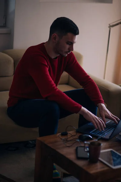 Müder Student tippt auf seinem Laptop und liest ein Buch, während er sitzt — Stockfoto