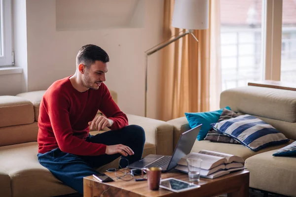 Müder Student tippt auf seinem Laptop und liest ein Buch, während er sitzt — Stockfoto