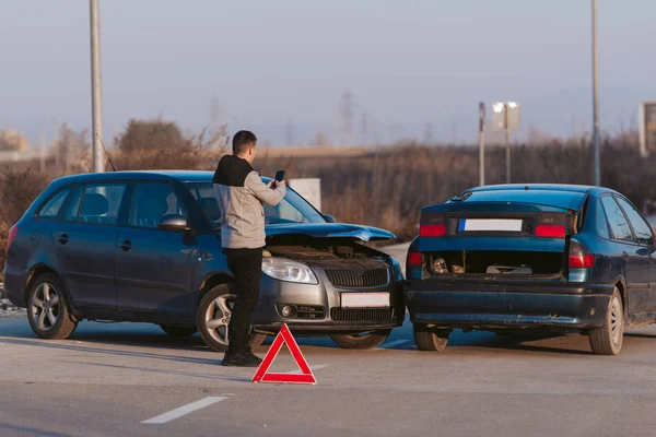 Мужчина фотографирует поврежденную синюю машину со смартфоном — стоковое фото