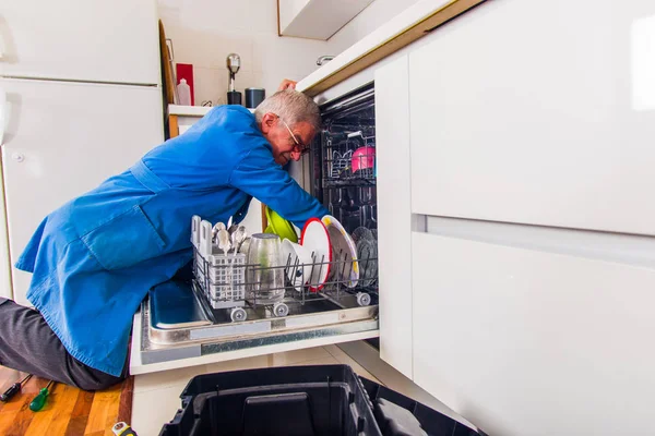 Senior serviceman fijación de la máquina lavavajillas en la cocina — Foto de Stock