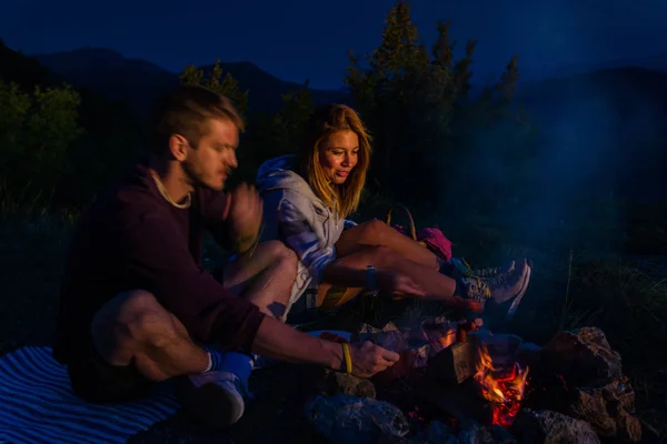 Young couple baking sausages on the campfire and drinking beer i — Stock Photo, Image