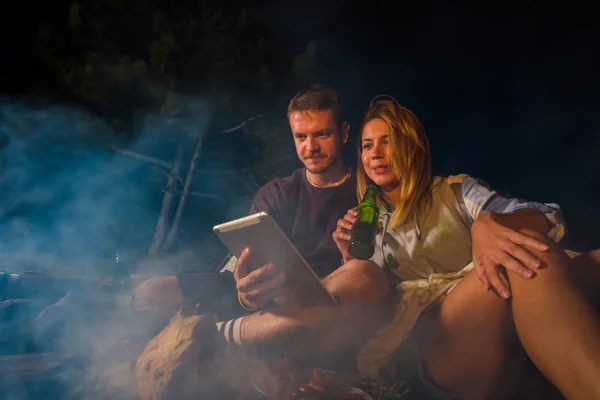 一对年轻夫妇在篝火上烤香肠，喝啤酒， — 图库照片