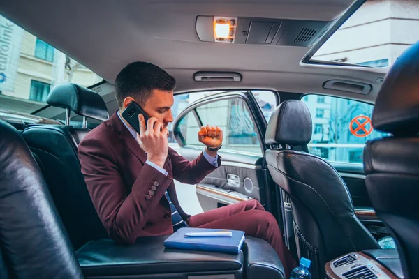 Empresario sentado en una limusina mientras habla por teléfono leyendo — Foto de Stock