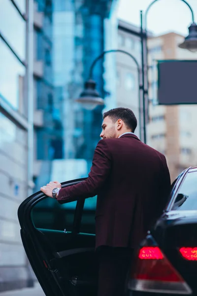 Bonito homem de negócios entrando e saindo de sua limusina enquanto olha — Fotografia de Stock