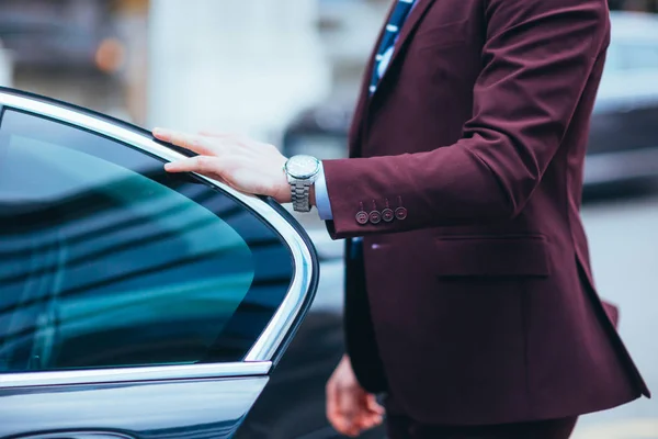 Empresario sosteniendo la puerta de su limusina mostrando su reloj un — Foto de Stock