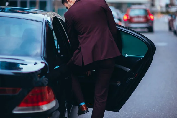 Bonito homem de negócios adequado entrando na parte de trás de sua limusina preta . — Fotografia de Stock