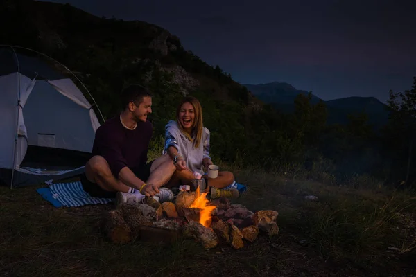 Young couple relaxing by the campfire and drinking coffee in the — Stock Photo, Image