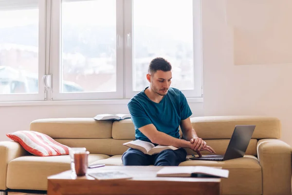 Schöner Student, der auf der Couch mit wenigen geöffneten Büchern studiert und — Stockfoto