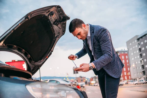 Jovem gerente formalmente vestido verificando seu carro óleo ao pôr do sol wh — Fotografia de Stock