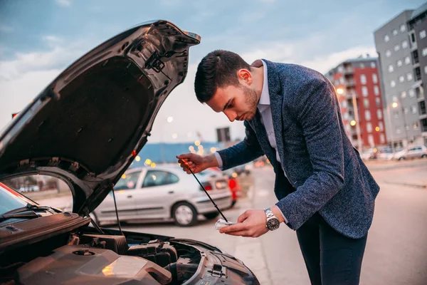 Mladý manažer formálně oblečen, kontrola jeho auta olej za západu slunce wh — Stock fotografie