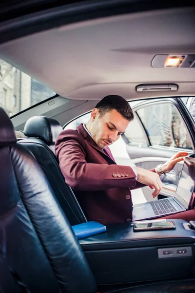 Homem de negócios usando lap top dentro de um carro de luxo — Fotografia de Stock