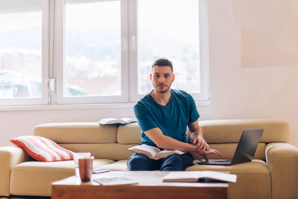 Schöner Student, der auf der Couch mit wenigen geöffneten Büchern studiert und — Stockfoto