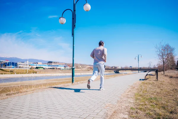 Atletisk ung man kör på en väg intill en flod medan slitage — Stockfoto