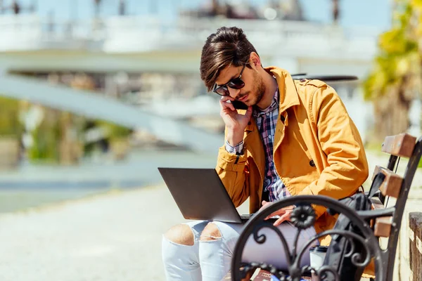 Junger Manager spricht am Handy und arbeitet auf seinem Laptop in der Stadt — Stockfoto