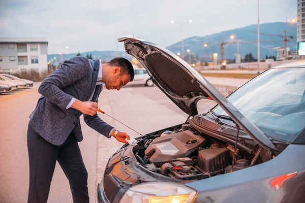 Fiatal vezető hivatalosan öltözött ellenőrzése az autó olajat, a naplemente wh — Stock Fotó