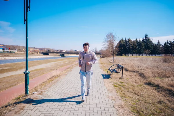 Sportieve jonge man loopt op een spoor naast een rivier terwijl slijtage — Stockfoto