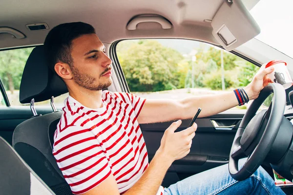 Fiatal férfi autóban mobil-és kávéval a kezében — Stock Fotó