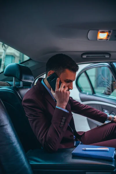 Empresario sentado en una limusina mientras habla por teléfono leyendo — Foto de Stock