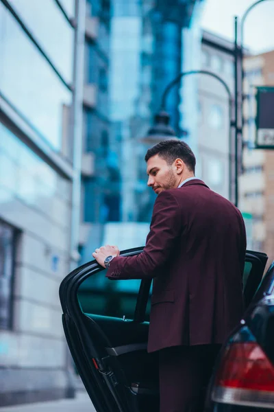 Bonito homem de negócios entrando e saindo de sua limusina enquanto olha — Fotografia de Stock