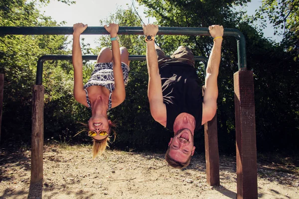 Couple doing exercises on high bars in forest gym — Stock Photo, Image