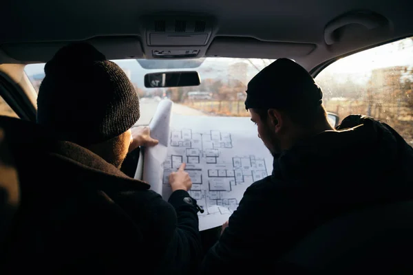 Zwei gewalttätige Räuber, die in einem Auto sitzen und einen Bauplan von t betrachten — Stockfoto