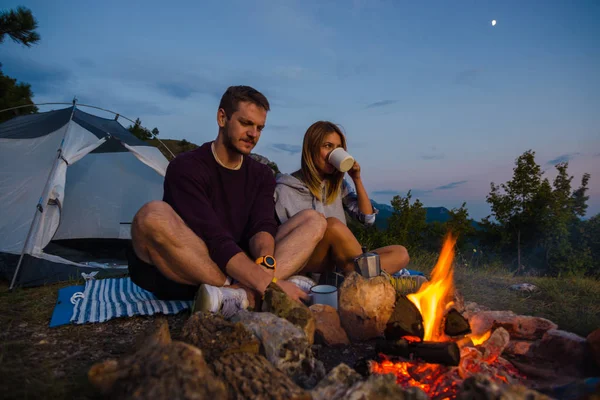 Casal jovem bebendo café, e aquecendo na fogueira em — Fotografia de Stock