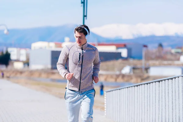 A panting athlete running fast on a track while wearing headphon — Stock Photo, Image