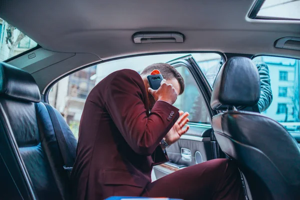 Empresario sentado en una limusina mientras habla por teléfono leyendo — Foto de Stock