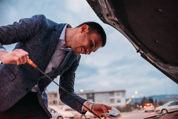 Mladý manažer formálně oblečen, kontrola jeho auta olej za západu slunce wh — Stock fotografie