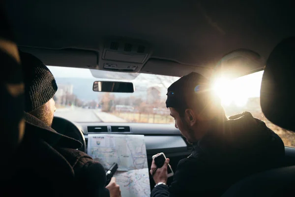 Criminales sentados al atardecer en un coche, mirando el mapa de la ciudad y — Foto de Stock