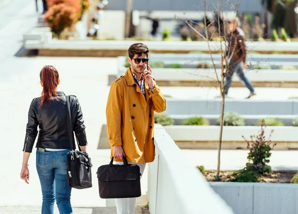 Empresário de casaco falando no smartphone no lugar urbano — Fotografia de Stock