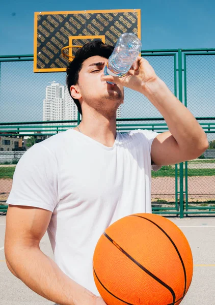 Ένας ισχυρός κακούτος άντρας είναι το πόσιμο νερό στο γήπεδο του μπάσκετ. — Φωτογραφία Αρχείου