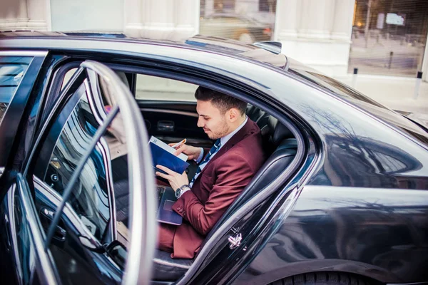 Empresário sorrindo verificando seu caderno dentro de um carro — Fotografia de Stock