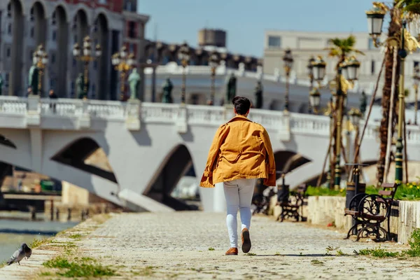 Empresário urbano com casaco amarelo caminhando perto do rio — Fotografia de Stock