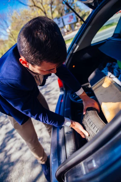 Empresário barbudo (empreendedor) está desempacotando seu pneu sobressalente — Fotografia de Stock