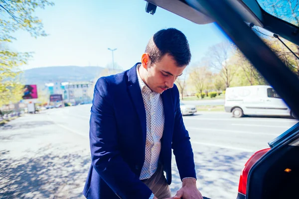 Ein müder Geschäftsmann holt an einem sonnigen Tag einen Reifen aus seinem Auto — Stockfoto