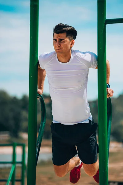 Atractivo atlético haciendo ejercicio pull-up en el parque de verano ou —  Fotos de Stock