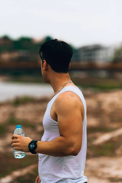 Jonge sport mannelijke atleet drinkwater staande in de natuur — Stockfoto